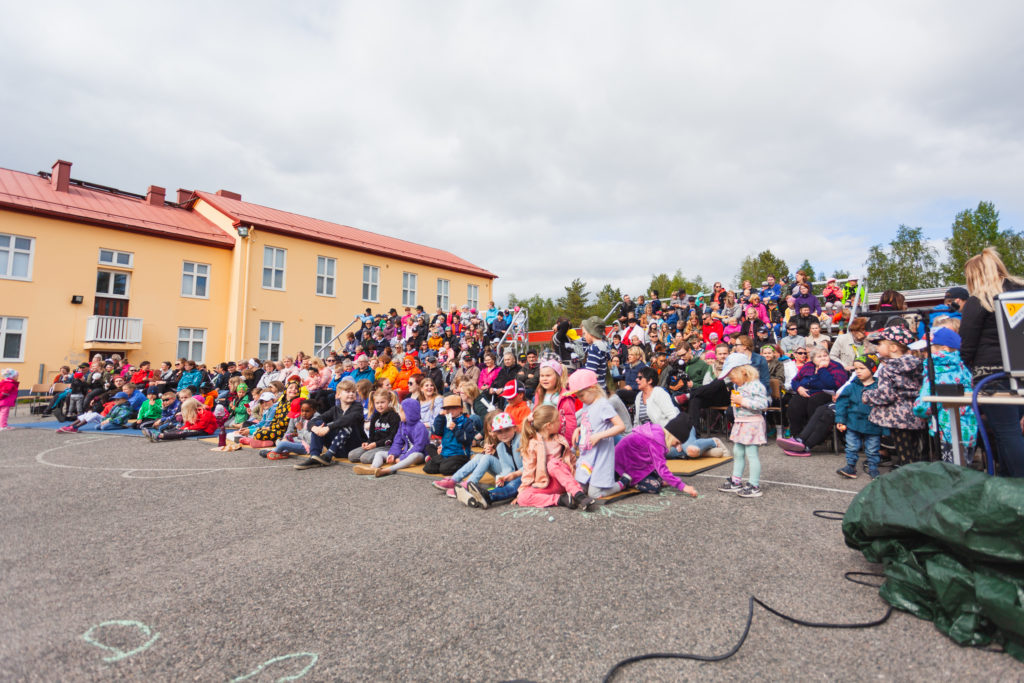 Yleisöä Kolarin lukion pihalla sekä asfaltilla, tuoleilla, että nousevassa katsomossa. Sää on kirkas ja pilvinen, taustalla näkyy hieman keltaista lukiorakennusta.