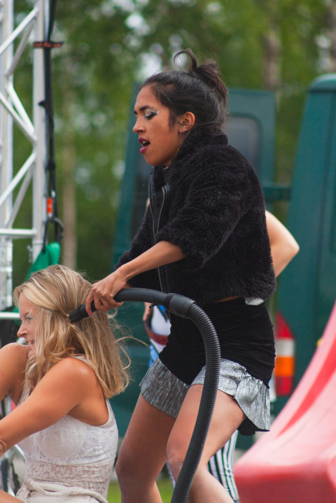 Mustaan pukeutunut nainen imuroi vaaleaan pukeutuneen naisen hiuksia sirkusesityksessä.